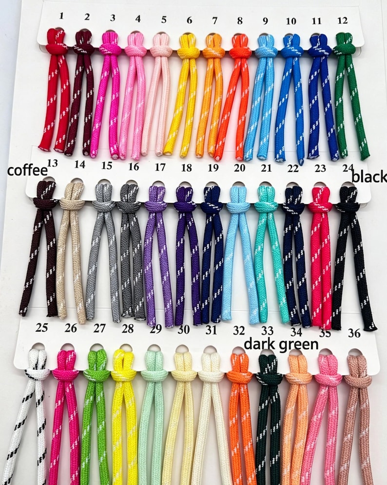 May include: A color chart featuring thirty-six numbered pairs of nylon cords, each with a reflective white diagonal stripe. The cords are arranged in three rows on a white display card, showcasing a variety of colors including red, pink, yellow, blue, green, purple, and black.