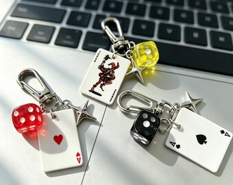 May include: Three keychains featuring silver-toned lobster clasps and star charms. One keychain has a red die and an Ace of Hearts card. Another has a yellow die and a Joker card. The third has a black die and an Ace of Spades card.