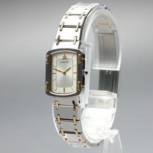 May include: A Credor wristwatch featuring a rectangular silver dial with gold-tone hands and indices. The watch case and link bracelet are constructed from two-tone silver and gold metal, showcasing a polished finish with a secure clasp mechanism.