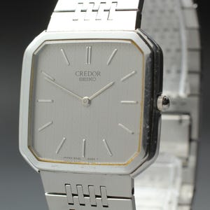 May include: A silver Credor Seiko watch with a rectangular face and a silver band. The watch face is light gray with silver hands and markers. The watch has a small crown and the text "Credor Seiko" is printed on the face.