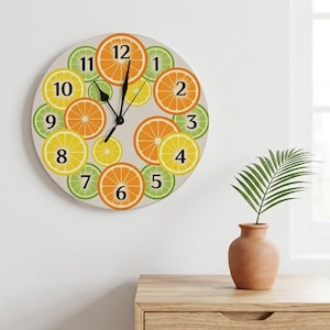 May include: A round wall clock featuring a light gray background decorated with a pattern of sliced oranges, lemons, and limes. The clock face displays black numbers from 1 to 12 and includes two black hands to indicate the time of day.