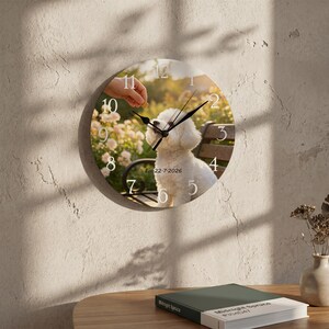 Könnte beinhalten: Eine runde Wanduhr mit einem Fotodruck eines weißen Bichon Frise Hundes, der draußen auf einer Bank sitzt. Das Zifferblatt zeigt schwarze Zeiger, weiße Ziffern von 1 bis 12 und den aufgedruckten Text Est 22-7-2026.