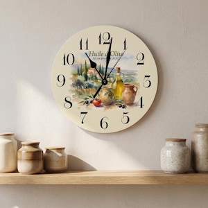 May include: A round wall clock with a cream-colored face featuring black numerals and a watercolor illustration of a landscape with olive oil bottles, a tomato, and olives. The text Huile d'Olive Aix en provence AOC is printed in black.