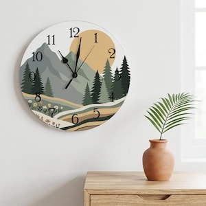 May include: A round wall clock featuring a printed landscape illustration of grey mountains, a large tan sun, dark green pine trees, and a foreground of rolling hills with small flowers. The clock has black numerals and black hour and minute hands.