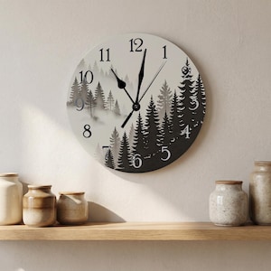 Könnte beinhalten: Eine runde Wanduhr mit einer schwarz-weißen Waldlandschaft und nebligen Kiefern. Das Zifferblatt zeigt schwarze arabische Ziffern von 1 bis 12 und verfügt über schwarze Stunden-, Minuten- und Sekundenzeiger in der Mitte.