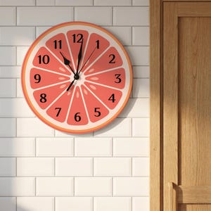 May include: A round wall clock featuring a graphic design of a sliced grapefruit with a pink interior and orange rind. The clock face displays black numbers from one to twelve arranged in a circle, with black hour, minute, and second hands.