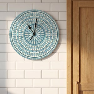 May include: A round wall clock featuring a blue and white mandala-inspired pattern with concentric circles of oval shapes. The clock has two black hands positioned at the centre, set against a light blue and white background with a radial design.