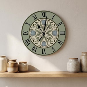 Könnte beinhalten: Eine runde Wanduhr mit einem salbeigrünen Zifferblatt, schwarzen römischen Ziffern und einem zentralen kreisförmigen Muster aus blauen Tulpen und kleinen weißen Blüten. Die Uhr hat schwarze Zeiger für Stunden, Minuten und Sekunden.