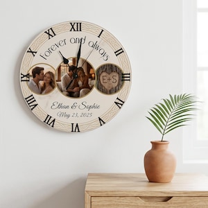 May include: A round wall clock with a cream-colored face, black Roman numerals, and a braided border. It features the text Forever and always, Ethan & Sophie, and May 23, 2025. Three circular photo inserts display a couple and a heart carved in a tree.