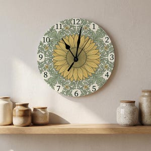 May include: A round wall clock featuring a large yellow sunflower at its center, surrounded by a green and cream botanical leaf pattern. The clock face displays black Arabic numerals from 1 to 12 and has two black hands for timekeeping.