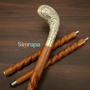 Op de afbeelding: Een houten wandelstok met een zilverkleurige, sierlijke handgreep. De schacht van de stok is bruin met een gedraaid ontwerp. De handgreep heeft een gegraveerd bloemmotief. De tekst "Simrupa" is zichtbaar.