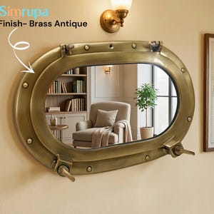 Puede incluir: Espejo ojo de buey con acabado de latón antiguo. El espejo ovalado está montado en una pared con acabado de latón. El espejo tiene un tema náutico y está rodeado por un marco de latón con remaches y un asa. El texto "Simrupa" y "Finish- Brass Antique" son visibles.