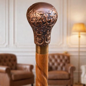 May include: A decorative walking cane with a copper-colored, floral-patterned handle and a wooden, twisted shaft. The handle has a rounded top and a brass collar. The cane is a classic accessory.
