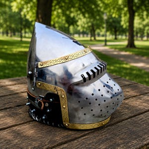 Könnte beinhalten: Ein polierter mittelalterlicher Helm aus Stahl mit Messingdetails. Der Helm hat eine spitze Krone, ein perforiertes Visier und dekorative Messingverzierungen. Ein Lederriemen ist sichtbar. Der Helm steht auf einer Holzoberfläche.
