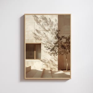 May include: A framed print featuring a sepia-toned architectural scene. The image showcases a building with a textured, light-colored facade, a window, and a small tree. Shadows from the tree's leaves are cast on the wall.