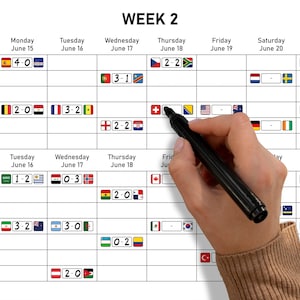 May include: A white FIFA World Cup Week 2 schedule grid featuring rows for times and columns for dates. The chart displays various national flags and match scores in rectangular boxes. A black marker is positioned over a blank score box on the grid.