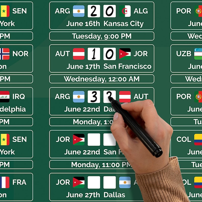 May include: A green chalkboard displaying a schedule of soccer matches with team flags, dates, times, and scores. A hand holding a black marker is pointing at the board. The board includes the text "June 16th Kansas City" and "June 17th San Francisco".