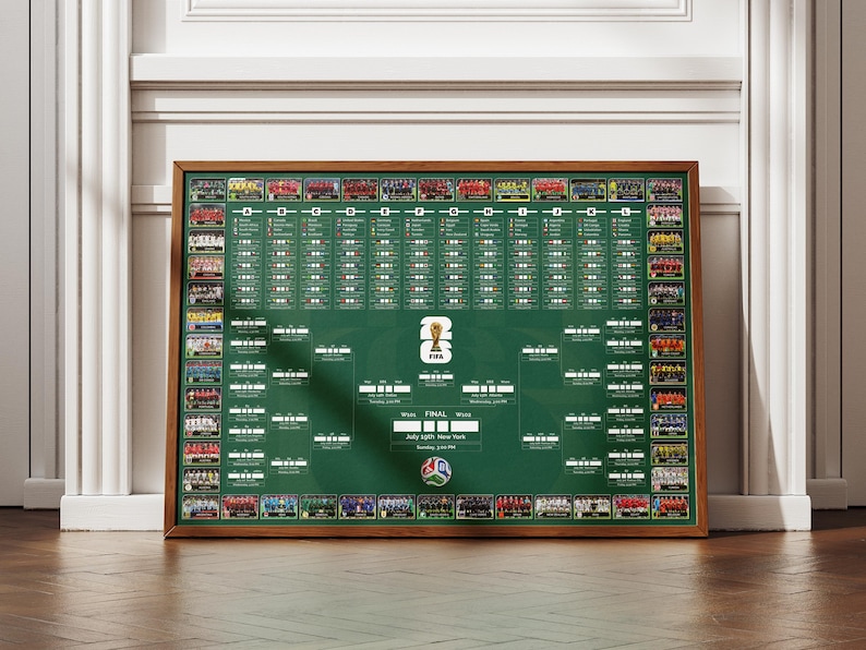 May include: A framed green chart with team photos and a tournament bracket. The chart has a wooden frame and features the FIFA logo and text indicating the final location and date. The chart is displayed against a white wall.