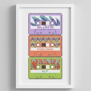 May include: A framed print featuring three colorful cassette tapes. Each tape has a unique design and text: "Take a Chill Pill," "Totally Tubular," and "As If!" The tapes are in shades of purple, orange, and green, with white text and accents.