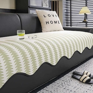 May include: A black leather sofa with a patterned cover featuring a repeating green and white design. A decorative pillow with the words "LOVE HOME" is on the sofa. A glass of liquid and a pair of sandals are also visible.