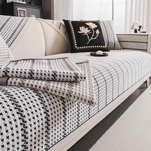 May include: A modern sofa with a white frame and patterned cushions and throw blankets. The cushions and throw blankets feature a black and white geometric design. A black pillow with a floral design is also visible.