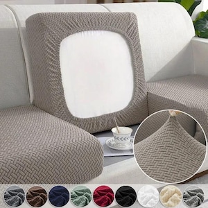 May include: A grey, textured sofa cushion cover with a woven pattern. The cover is stretched over a cushion, demonstrating its elasticity. A variety of colour options are displayed at the bottom of the image, including grey, brown, and black.