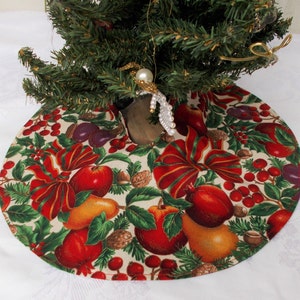 May include: A round Christmas tree skirt with a festive fruit and bow pattern. The skirt features red apples, pears, plums, and holly berries on a cream background. Red bows with green stripes add to the holiday design.