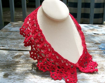 May include: A bright red crocheted collar featuring an intricate openwork lace pattern with a scalloped edge. The collar is secured at the front with a small, matching red button, creating a decorative accessory that drapes around the neck area.