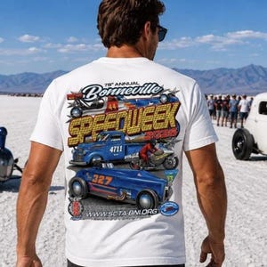 Könnte beinhalten: Weißes T-Shirt mit einem farbenfrohen Grafikdesign für die 78. jährliche Bonneville Speedweek 2026. Das Design zeigt Oldtimer-Rennwagen, Motorräder und den Text "Speedweek". Das T-Shirt wird von einer Person getragen.