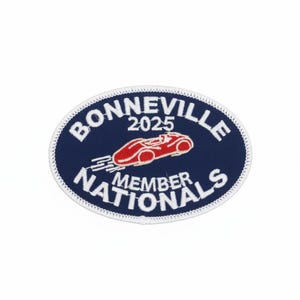 Peut inclure: Écusson ovale avec un fond bleu marine et du texte blanc brodé. Le texte indique "BONNEVILLE 2025 MEMBER NATIONALS". Un dessin de voiture de course rouge est au centre. L'écusson a une bordure blanche.