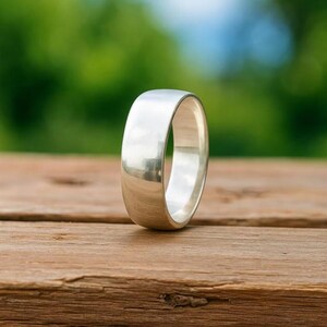 Puede incluir: Un anillo de banda de color plateado pulido con una superficie exterior lisa y redondeada y un acabado metálico reflectante. El anillo presenta una construcción simple y sólida con un ancho constante en toda la circunferencia del aro.