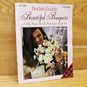 May include: A pink and white book titled "Bride's Guide to Beautiful Bouquets" with a photo of a woman holding a bouquet of flowers. The book cover includes the text "12 Wedding Bouquets You Can Make for your Special Day" and "By Betty Valle".