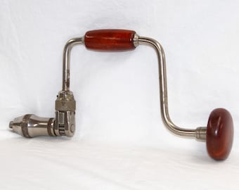 May include: A silver brace hand drill with wooden handles. The drill has a crank handle and a chuck for holding drill bits.