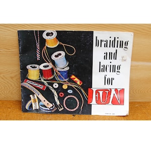May include: A book titled "Braiding and Lacing for FUN" with a black background and colorful spools of thread, cords, and braided items.