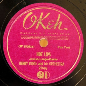 May include: A pink vinyl record label with gold lettering. The label reads "OKeh", "Registered U.S. Patent Office", "(W 152614)", "Fox Trot", "HOT LIPS", "-Busse-Lange-Davis-", "HENRY BUSSE and his ORCHESTRA", and "2846".