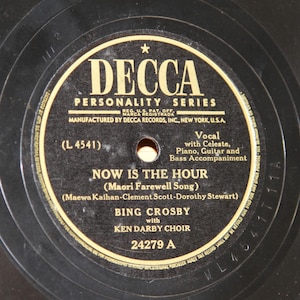 May include: A black and white vinyl record with a gold label. The label features the text "Decca Personality Series" and "Now Is The Hour (Maori Farewell Song)". The record is by Bing Crosby with Ken Darby Choir and has the catalog number 24279 A.