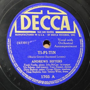 May include: A vintage vinyl record with a blue and gold label. The label features the text "DECCA" and the song title "TI-PI-TIN" by The Andrews Sisters. The record is a 78 RPM, with the catalog number 1703 A.