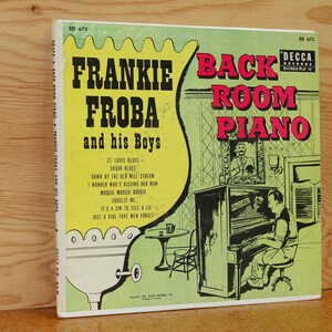 May include: Vintage vinyl record album cover for "Frankie Froba and his Boys" featuring "Back Room Piano." The cover is predominantly green and yellow with red text. The artwork depicts a man playing a piano in a room with a framed portrait.