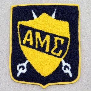 May include: A yellow and blue embroidered patch with the letters "AMZ" inside a shield shape. Two white swords are crossed behind the shield.