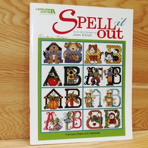 May include: A book titled "SPELL it out" with cross stitch designs by Joan Elliott. The cover features a colorful alphabet with different animal and nature-themed illustrations.