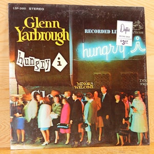 May include: A vintage vinyl record album cover featuring a photo of a crowd of people standing in line outside a restaurant with a neon sign that reads "hungry i". The album cover is titled "Glenn Yarbrough hungry i" and has a price tag that reads "$3.87".