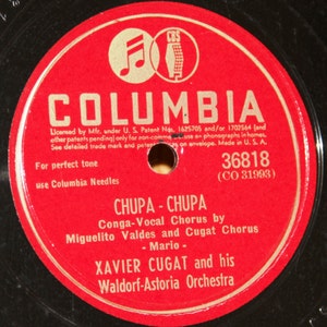 May include: Red vinyl record label with gold lettering. The label features the Columbia Records logo, the song title "CHUPA - CHUPA", the artist "XAVIER CUGAT and his Waldorf-Astoria Orchestra", and the song information "Conga-Vocal Chorus by Miguelito Valdes and Cugat Chorus - Mario -" along with the catalog number "36818 (CO 31993)".