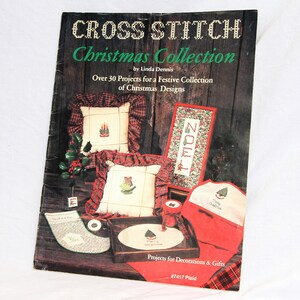 Peut inclure: Couverture d'un livre de point de croix pour Noël avec plus de 30 projets. La couverture présente une variété de motifs de point de croix, notamment une chaussette, un coussin, une pancarte et un arbre. Le livre est intitulé "Cross Stitch Christmas Collection" et est de Linda Dennis.