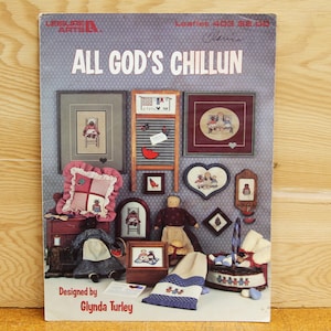 May include: A cross-stitch pattern booklet titled "All God's Chillun" featuring a variety of cross-stitch designs, including a pillow, a doll, a basket, and a washboard. The booklet is designed by Glynda Turley.