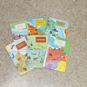 May include: A collection of six illustrated travel guide books featuring maps of various countries, including Italy, Spain, Northern Ireland, Bulgaria & Romania, Czechoslovakia, and Turkey. Each book has a colorful cover with a map and illustrations of landmarks and cultural elements.
