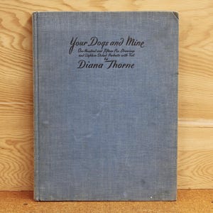 May include: A blue hardcover book titled "Your Dogs and Mine" by Diana Thorne. The book cover features the title in a cursive font and the subtitle "One Hundred and Fifteen Drawings and Eighteen Etched Portraits with Text" in a smaller font.