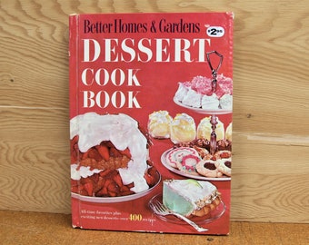 May include: A red cookbook titled "Better Homes & Gardens Dessert Cookbook" with a price tag of "$2.95". The cover features a variety of desserts, including a strawberry cake, a meringue pie, and a variety of cookies.