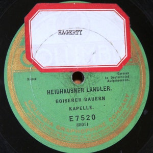 May include: A green vinyl record with a gold label. The label has the text "Columbia Graphophone Company" and "E7520" with the number "88011" below. The record is titled "Heidhausner Ländler" and features the text "Goiserer Bauern Kapelle". The record is labeled "German In Deutschland Aufgenommen."
