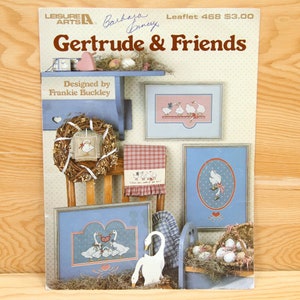 Peut inclure: Un livret de modèles de point de croix intitulé "Gertrude & Friends" conçu par Frankie Buckley. La couverture présente une variété de motifs de point de croix représentant des oies et une couronne.