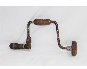 Puede incluir: Un taladro de mano vintage con mango de madera y manivela de metal. El taladro es de metal y tiene un acabado desgastado y oxidado.